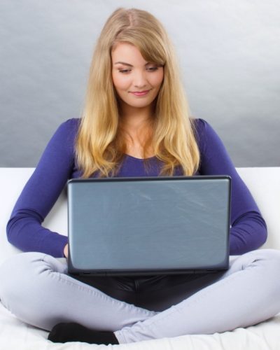 happy-woman-using-laptop-sitting-on-sofa-modern-PW877SD